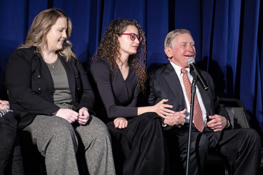 A panelist speaks into a microphone during the Criminal Justice Q&A event while two other panelists sit beside her on stage.