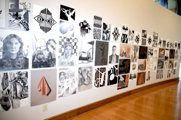 Gallery wall with rows of black-and-white and color art—portraits, abstracts, still lifes—above a wooden floor.
