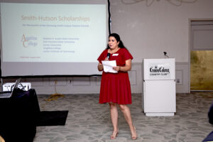 Woman in red dress speaks into mic before Smith-Hutson Scholarships presentation; laptop and projector in view.