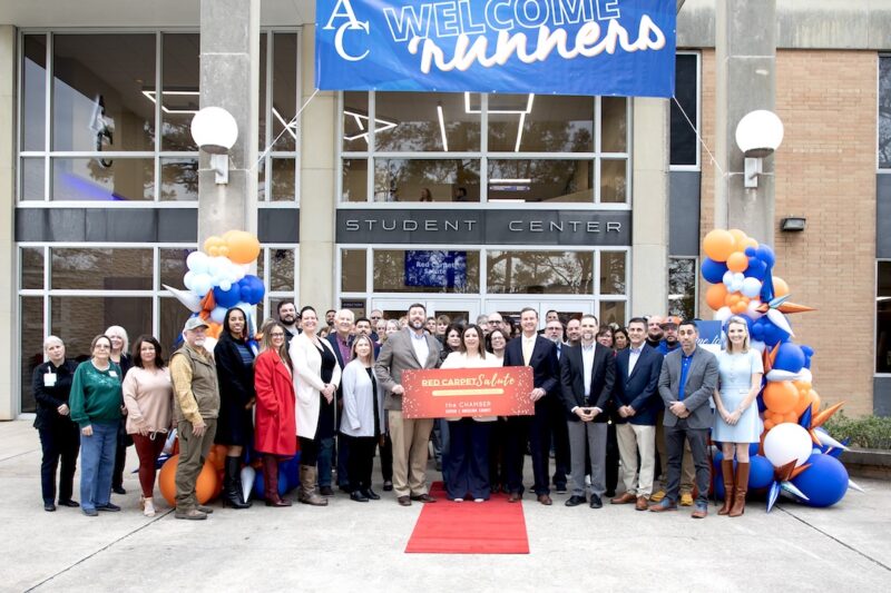 Group on red carpet outside student center with balloons, "Welcome Runners" banner, and large ribbon-cutting sign.