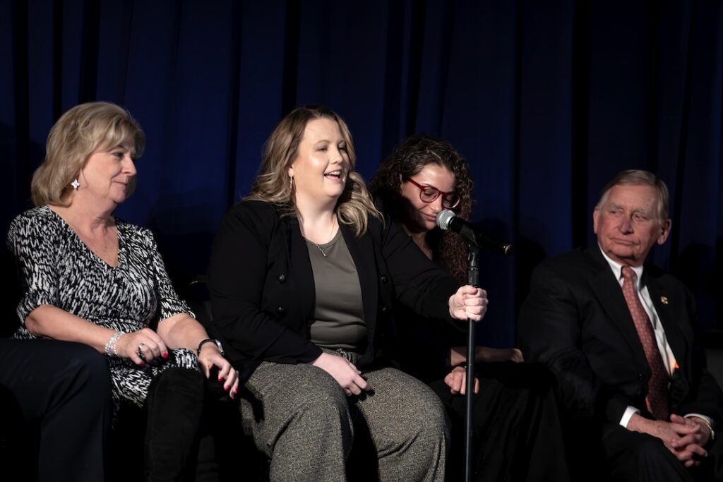 Panelists sit on stage during a Criminal Justice Q&A event as one woman speaks into a microphone, with other panelists listening beside her.