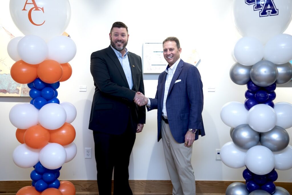 Two college leaders shake hands between Angelina College and SFA balloon columns during the Jacks Jumpstart partnership signing event.