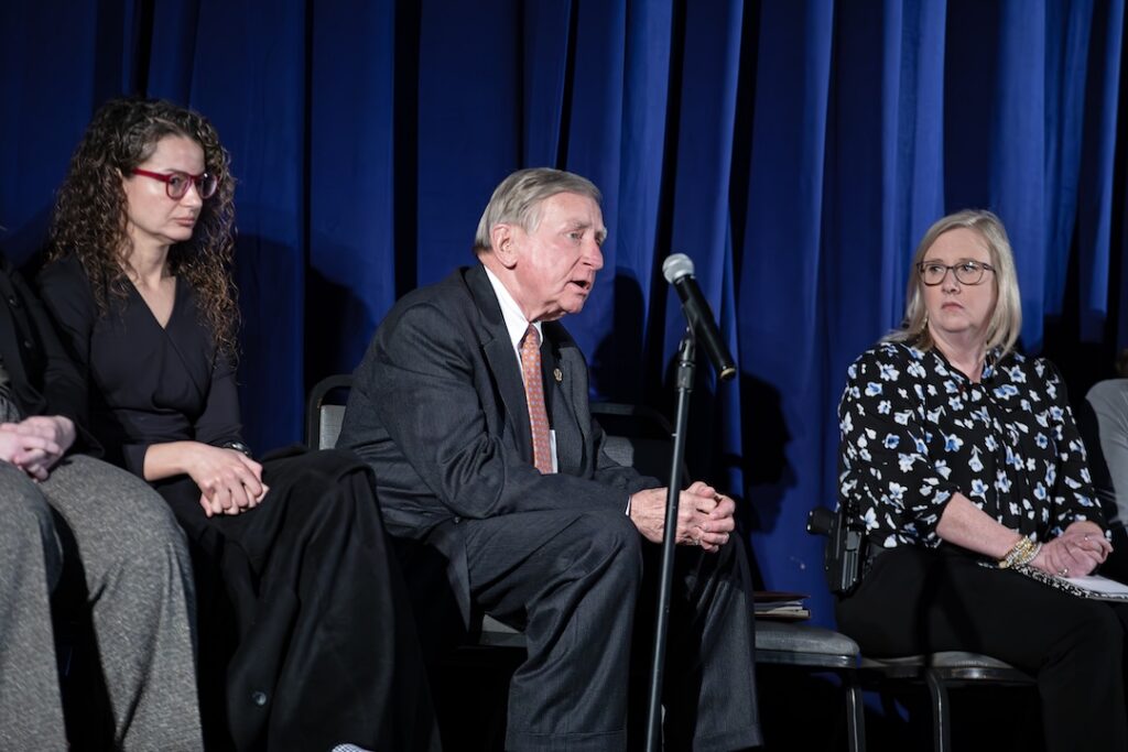 A panelist speaks into a microphone during the Criminal Justice Q&A event while two other panelists sit beside him on stage.