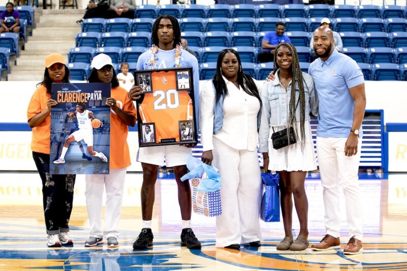Clarence Payia stands at center court during Sophomore Day recognition, holding a framed jersey and poster with family members beside him.