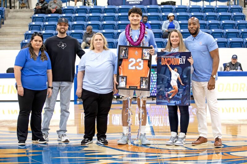 Daemon Ely poses at center court on Sophomore Day holding a framed No. 23 jersey and commemorative poster with family and coaches.