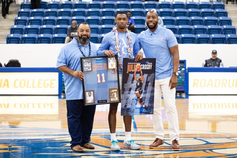 Julius Crosby stands with coaches during Sophomore Day recognition, holding a framed jersey and commemorative poster.