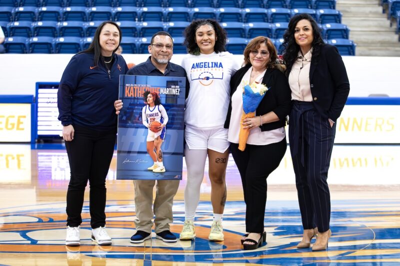 Katherine Martinez stands with family during Sophomore Day recognition, holding a player poster at center court.