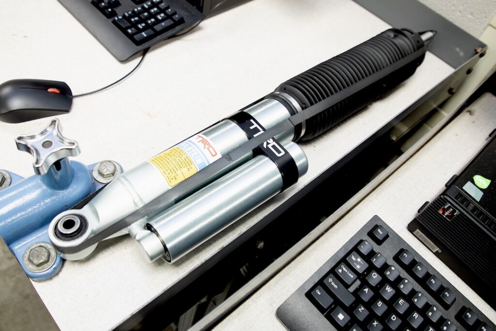 TRD-branded shock absorber with reservoir on a desk beside a keyboard, mouse, and office equipment.
