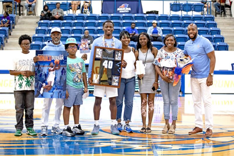 Ronald Durham is honored at center court on Sophomore Day, holding a framed No. 40 jersey and posing with family members.