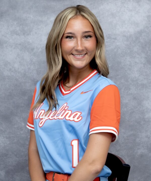 Smiling young woman with wavy blonde hair in a blue and orange Angelina softball jersey (#1), against a gray backdrop.