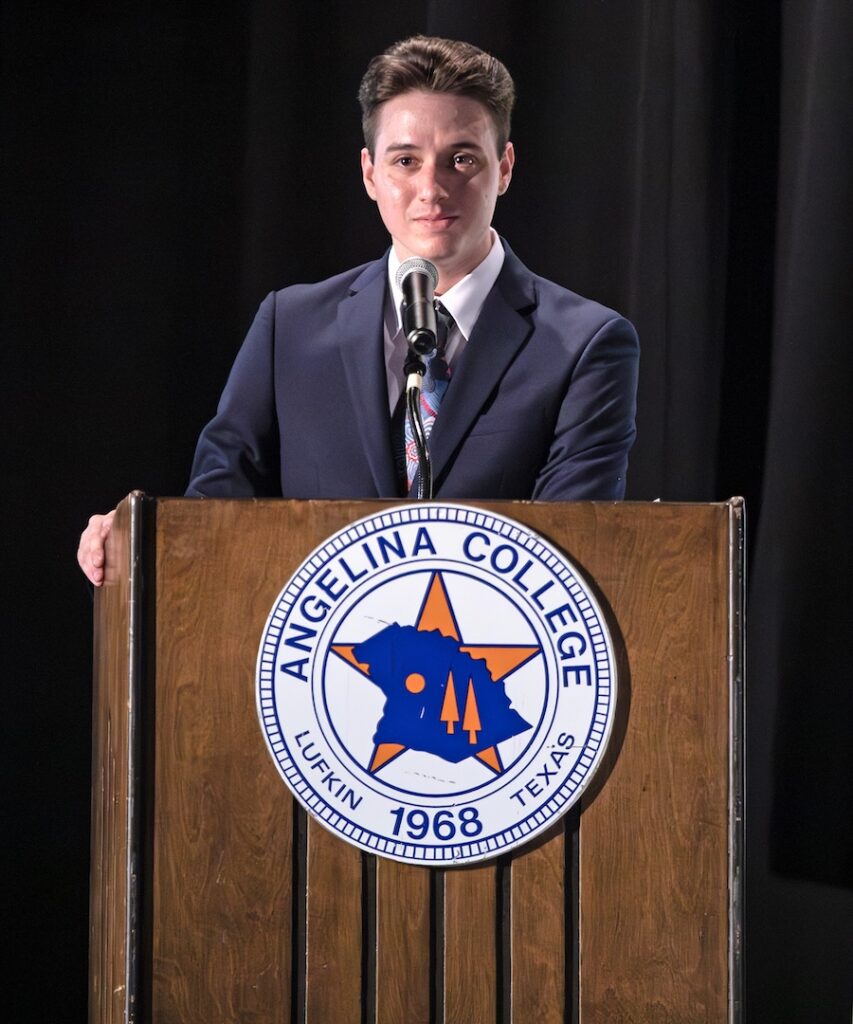 Person in a suit speaks at a podium with Angelina College seal showing a star, Texas map, and "Angelina College, Lufkin TX 1968.