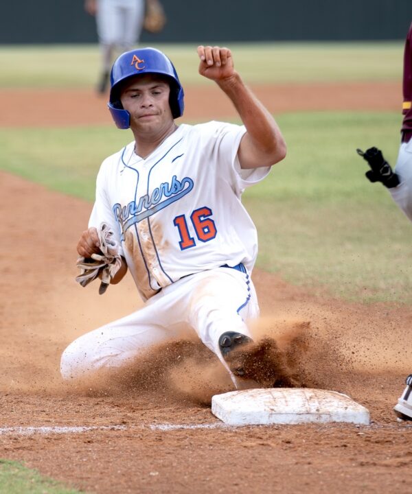 Baseball player in white uniform and blue helmet slides into a base, kicking up dirt with a determined expression.