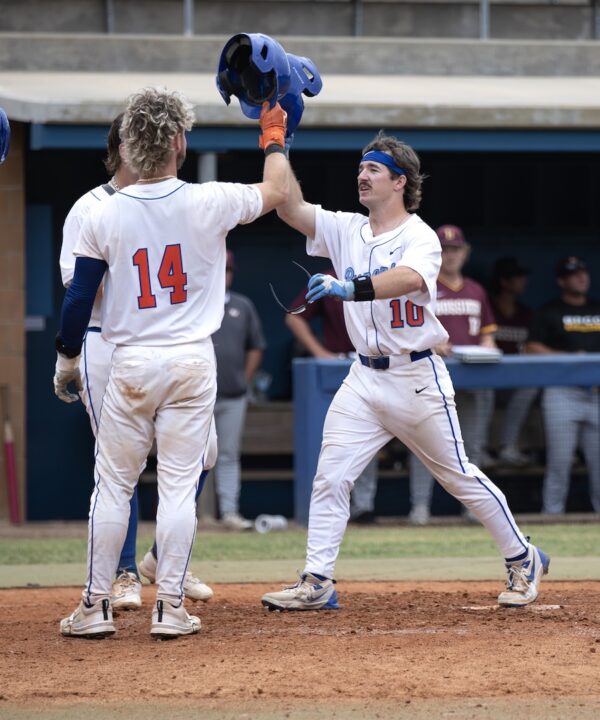 Baseball players 14 and 10 in white uniforms celebrate with a high-five as others watch from the dugout.