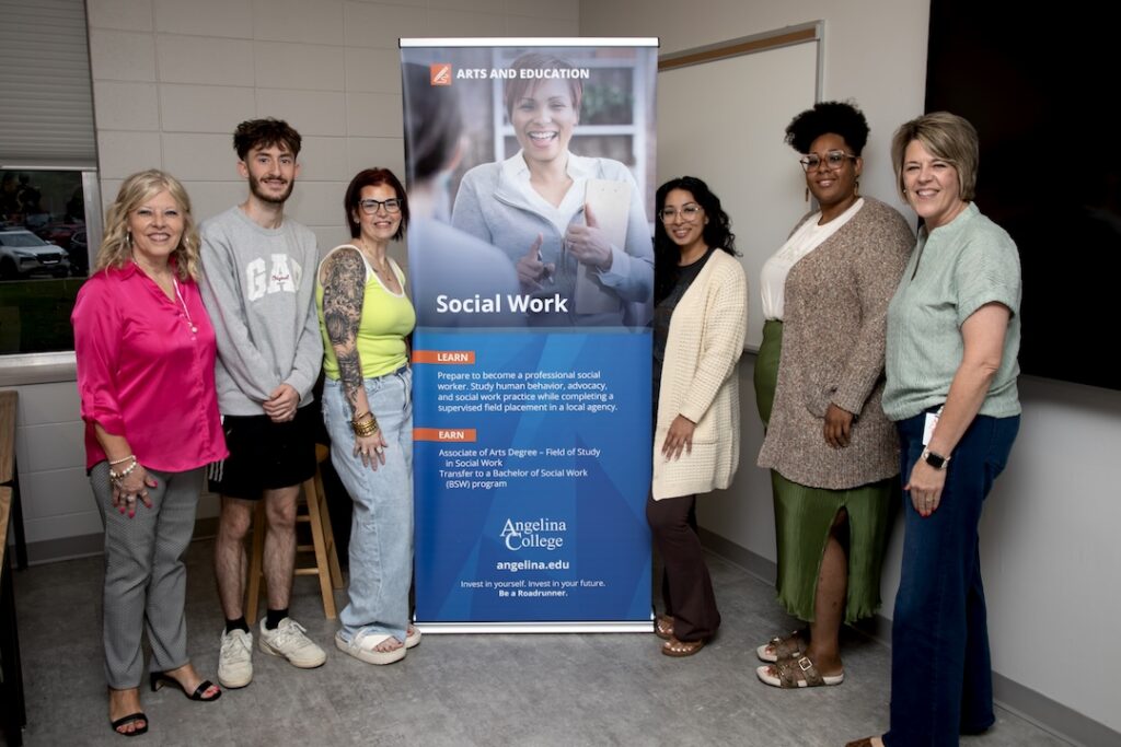 Six people smiling beside a banner for Angelina College’s Social Work program in a classroom, with program info and a woman’s photo.