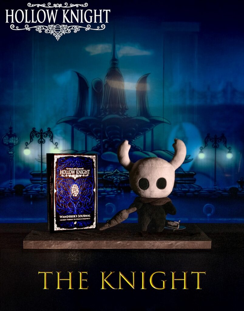 Plush Hollow Knight toy beside Wanderer's Journal on a platform, blue city backdrop, "Hollow Knight" and "The Knight" text.