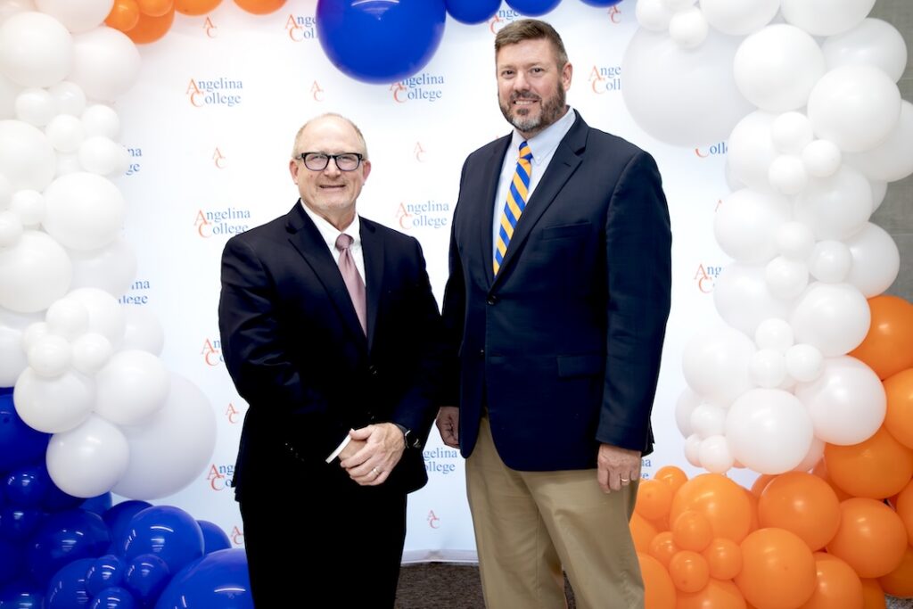 Two men in suits smile in front of an “Angelina College” logo backdrop, framed by blue, white, and orange balloons.