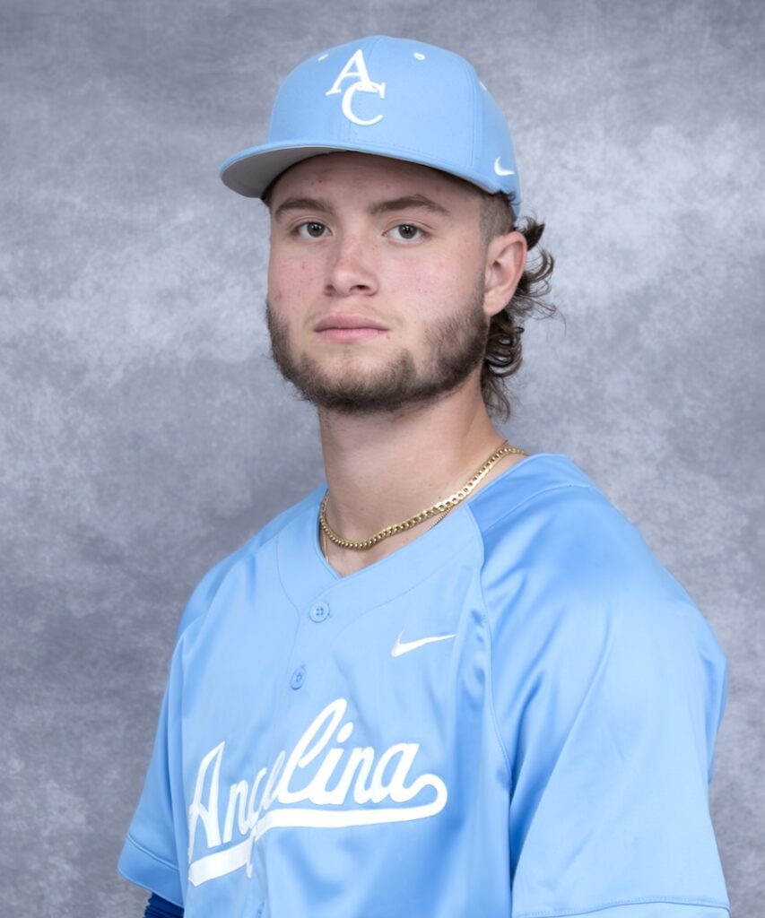 Young man in light blue baseball uniform and cap, trimmed beard, gold chain, neutral expression, gray textured background.