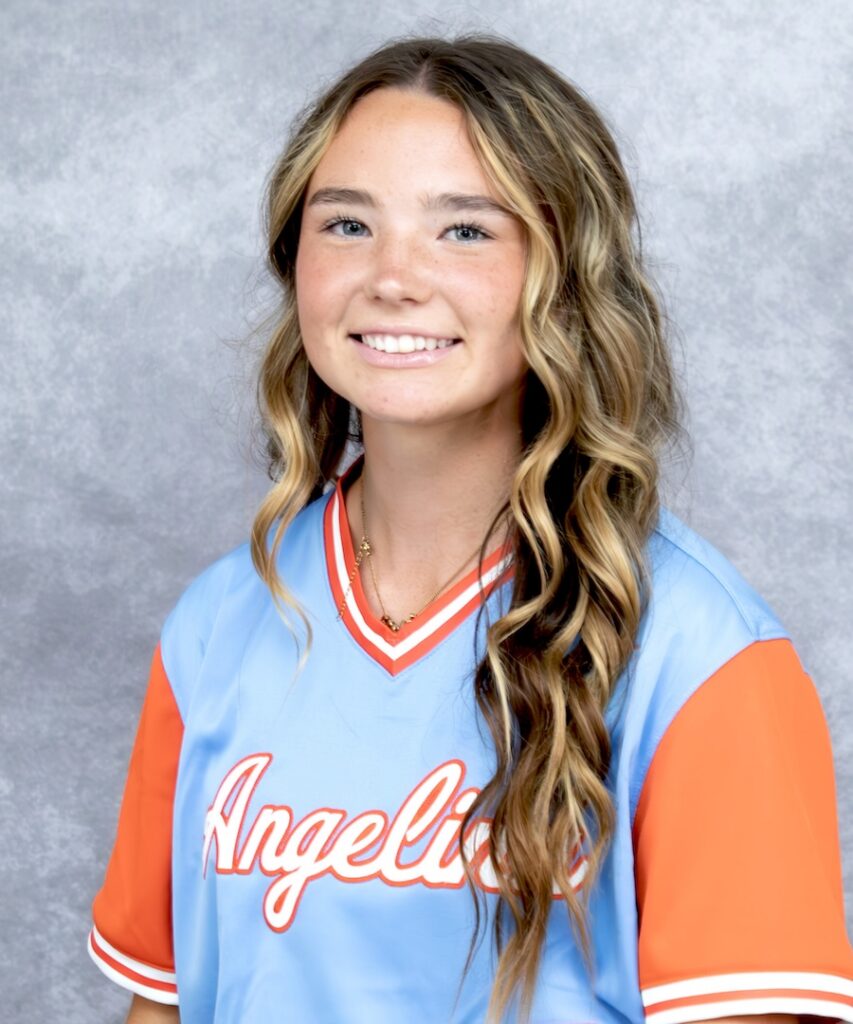 Young woman with long wavy blonde hair smiles, wearing a light blue and orange "Angelic" jersey, against a gray background.