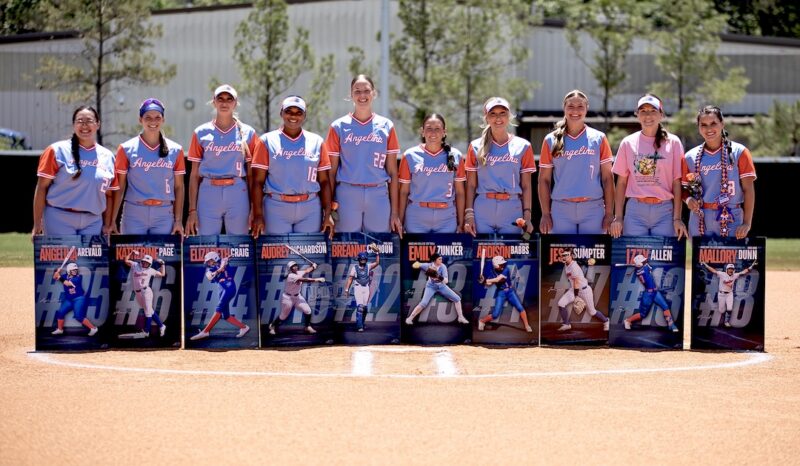 Ten softball players in blue and orange uniforms hold posters with their names, photos, and numbers. Trees and a building behind them.