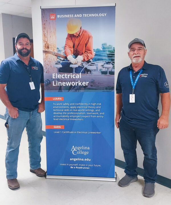 Two men in blue shirts and caps stand by an Angelina College Electrical Lineworker banner displaying program info and a worker in gear.