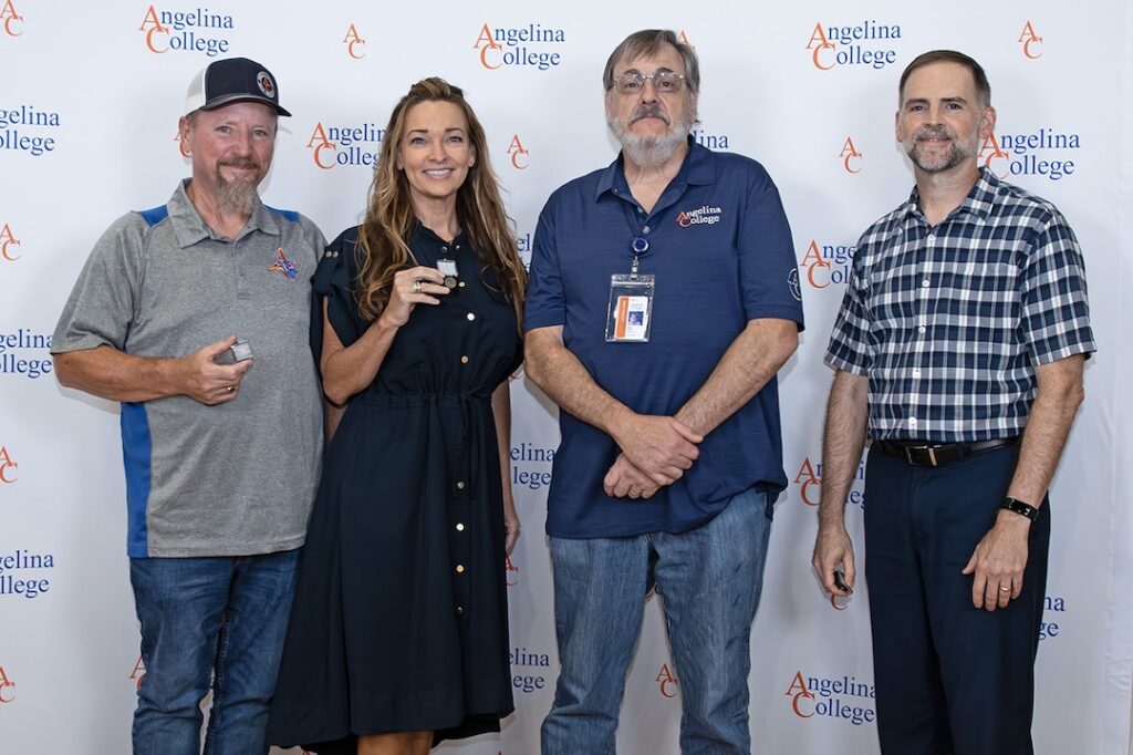 Four adults smiling in front of an Angelina College banner; three hold awards, dressed in business casual and polo attire.
