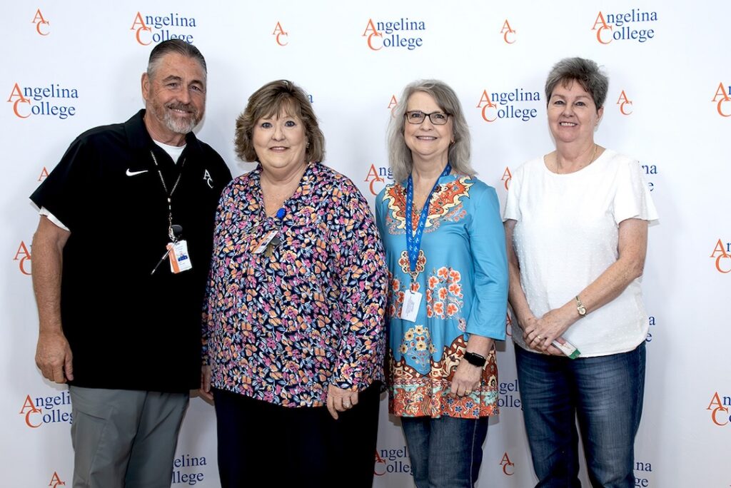 Four adults—three women and one man—smile in front of an Angelina College banner, dressed casually and business-casually.