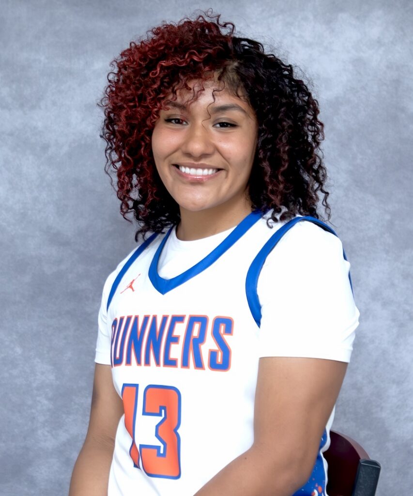 Smiling woman with curly hair in a white RUNNERS jersey, number 13, sits before a gray background.
