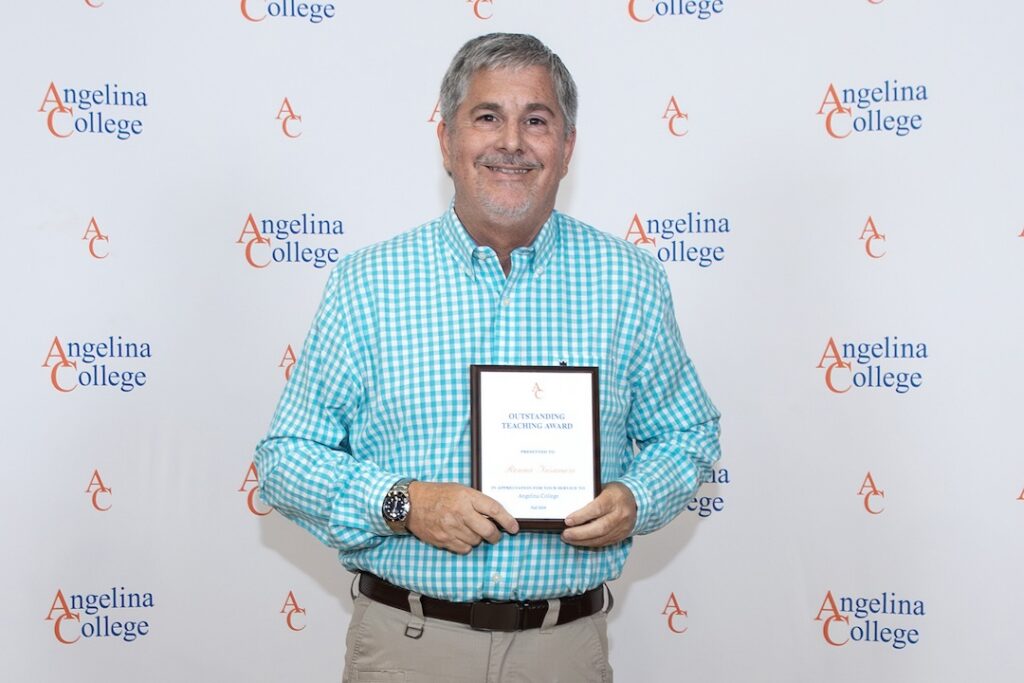 Smiling man in teal plaid shirt holds Outstanding Teaching Award in front of Angelina College logo backdrop.