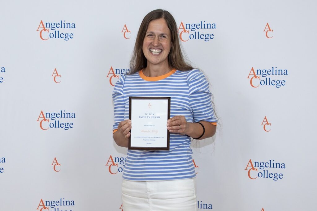 Smiling woman holds a faculty award plaque in front of an Angelina College backdrop with repeated AC letters.