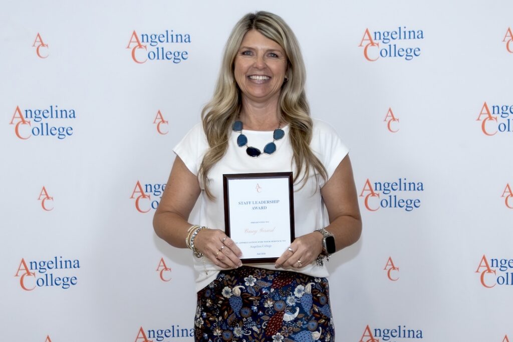 Smiling woman holds a Staff Leadership Award plaque in front of an Angelina College logo backdrop.