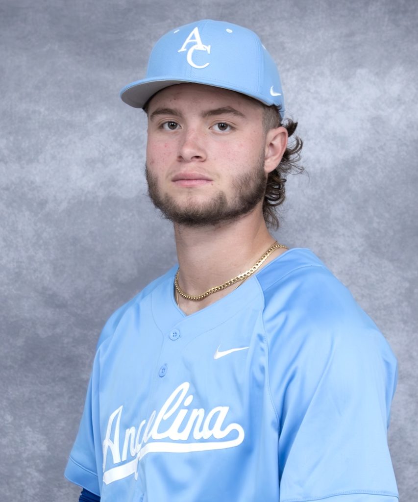 Young man with wavy hair, trimmed beard, and gold chain in a light blue baseball uniform and cap against a gray background.